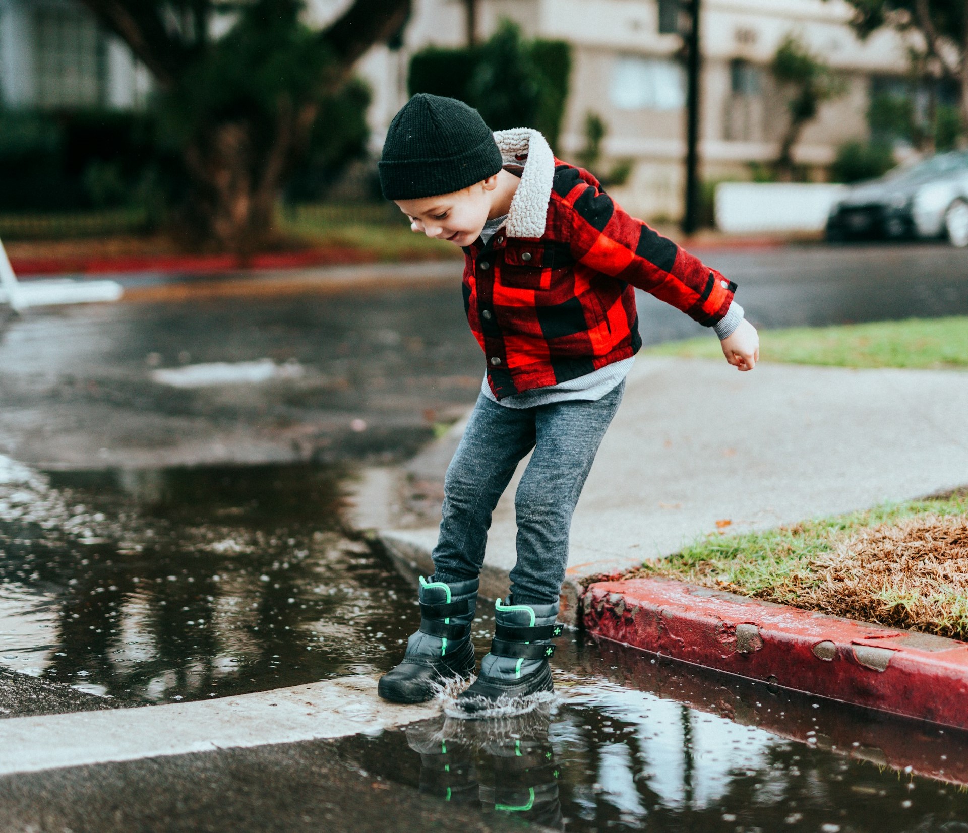 a child wearing boots happily jumping into a puddle